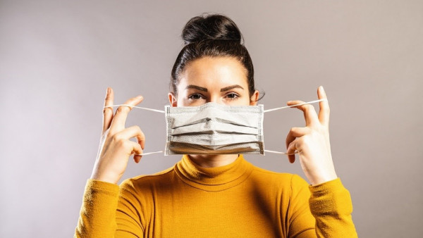 A person in a mustard roll-neck top is in the middle of putting on a mask.
